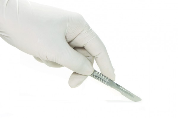 Scalpel in a hand with rubber glove on white background